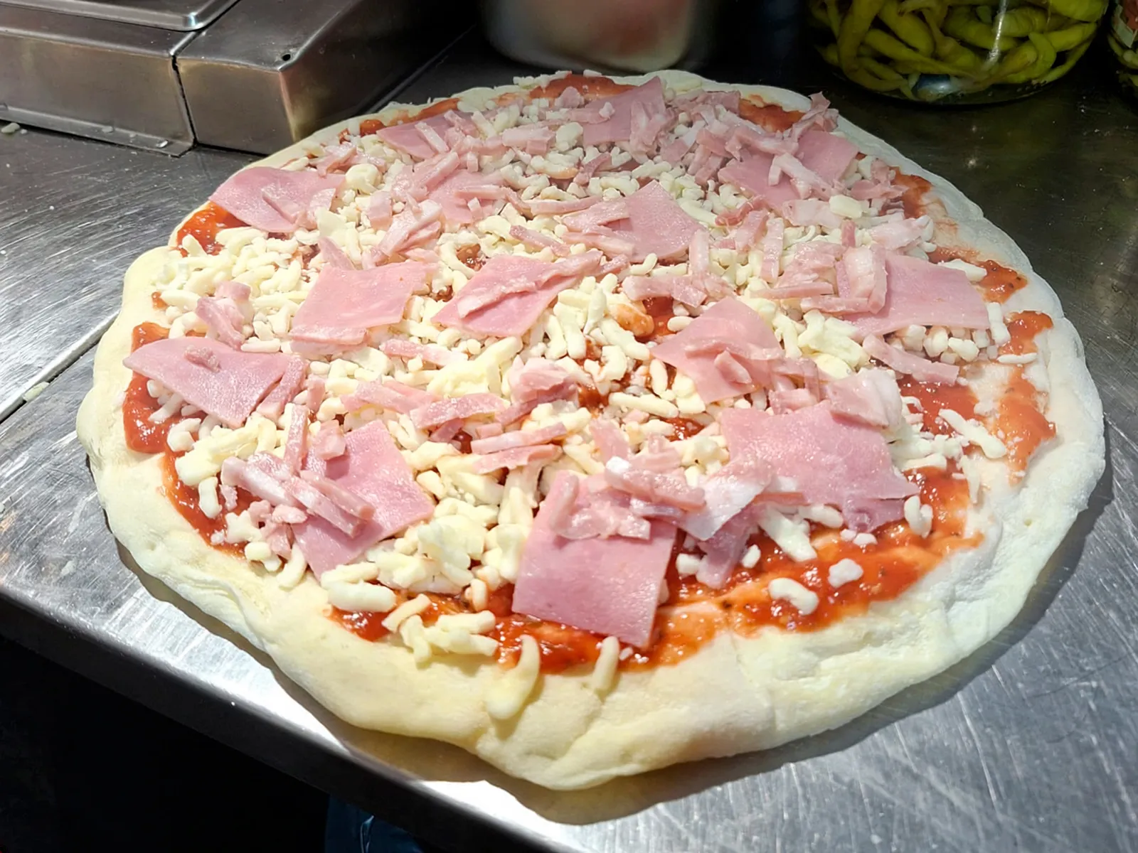 Una pizza recién montada con tomate, mozzarella y jamón, todavía cruda sobre la bandeja